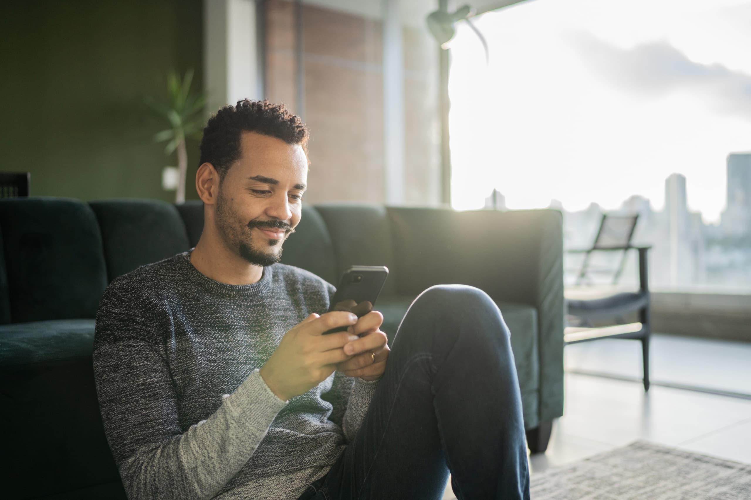 A man sitting in front of couch on cellphone